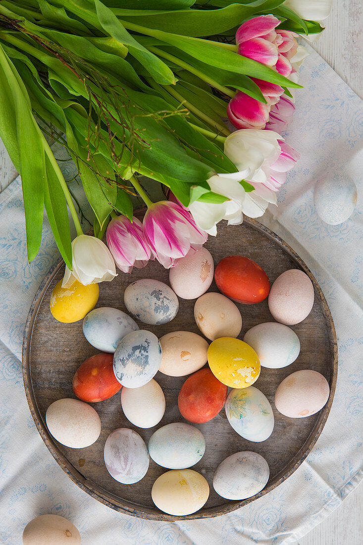 Colourful Easter eggs on a plate with a bunch of tulips