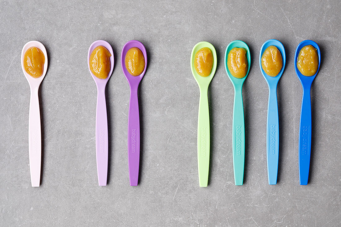 Baby food on colourful plastic spoons