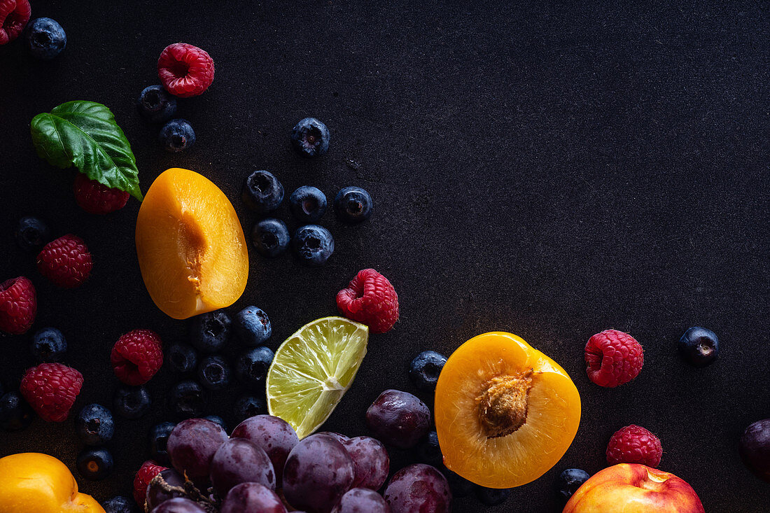 Fresh fruits and berries on dark background (Grapes, blueberries, raspberries with peaches and lime)