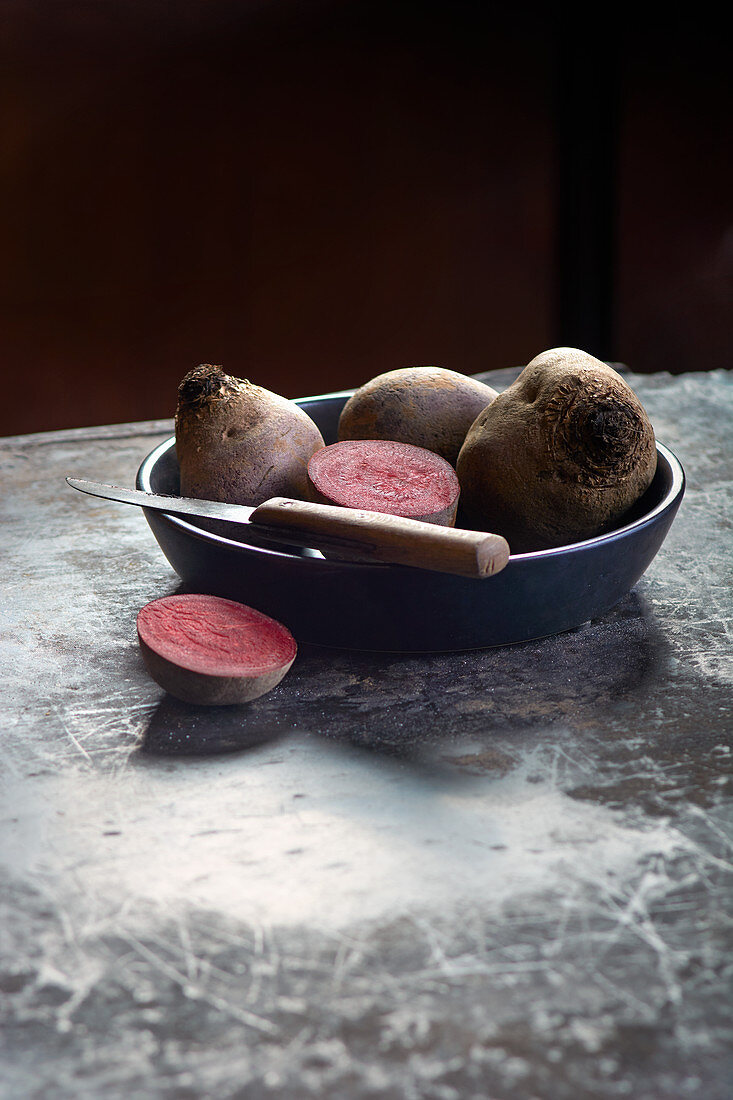 Beetroot, whole and halved, in a bowl with a knife