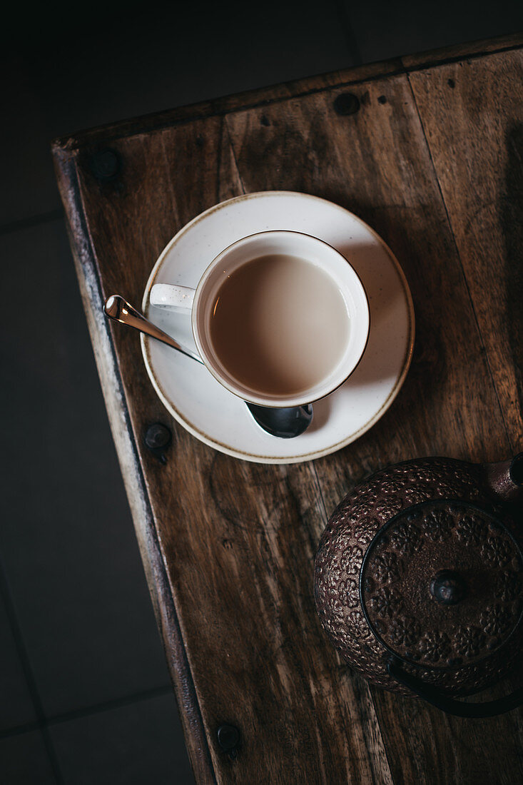 Eine Tasse Tee mit Milch und Metall-Teekanne auf Holztisch