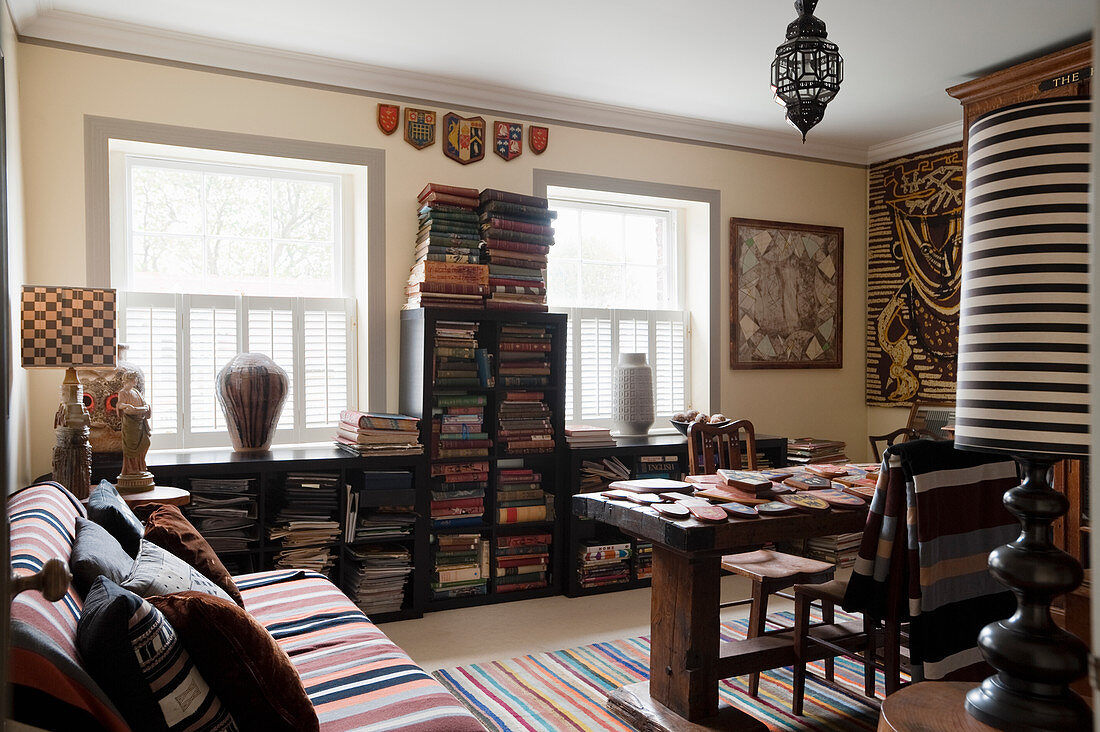 Striped sofa, rustic wooden table and bookcases below windows in living room