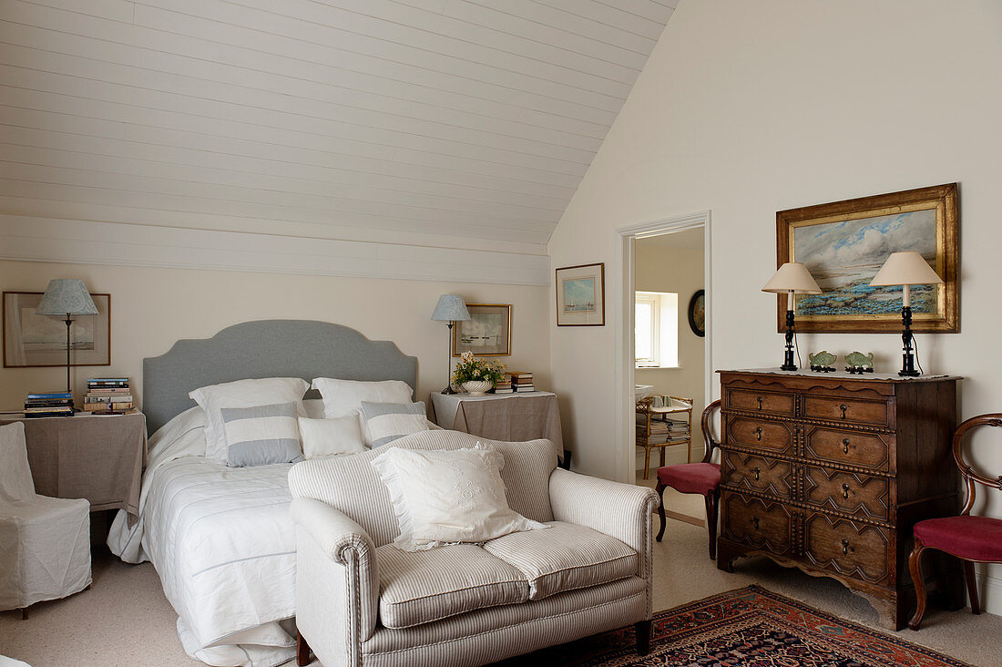 Leinenkissen und Bettbezug im Schlafzimmer mit antiker Kommode und kleinem Sofa