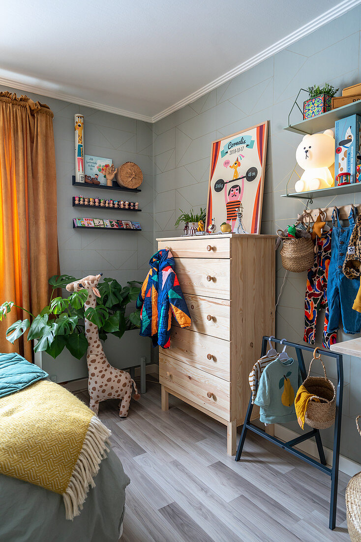 Baby clothes and chest of drawers in room with pale grey walls