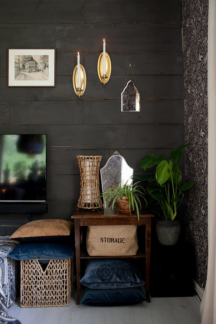 Table, basket, cushions and plants on floor below decorations on black board wall