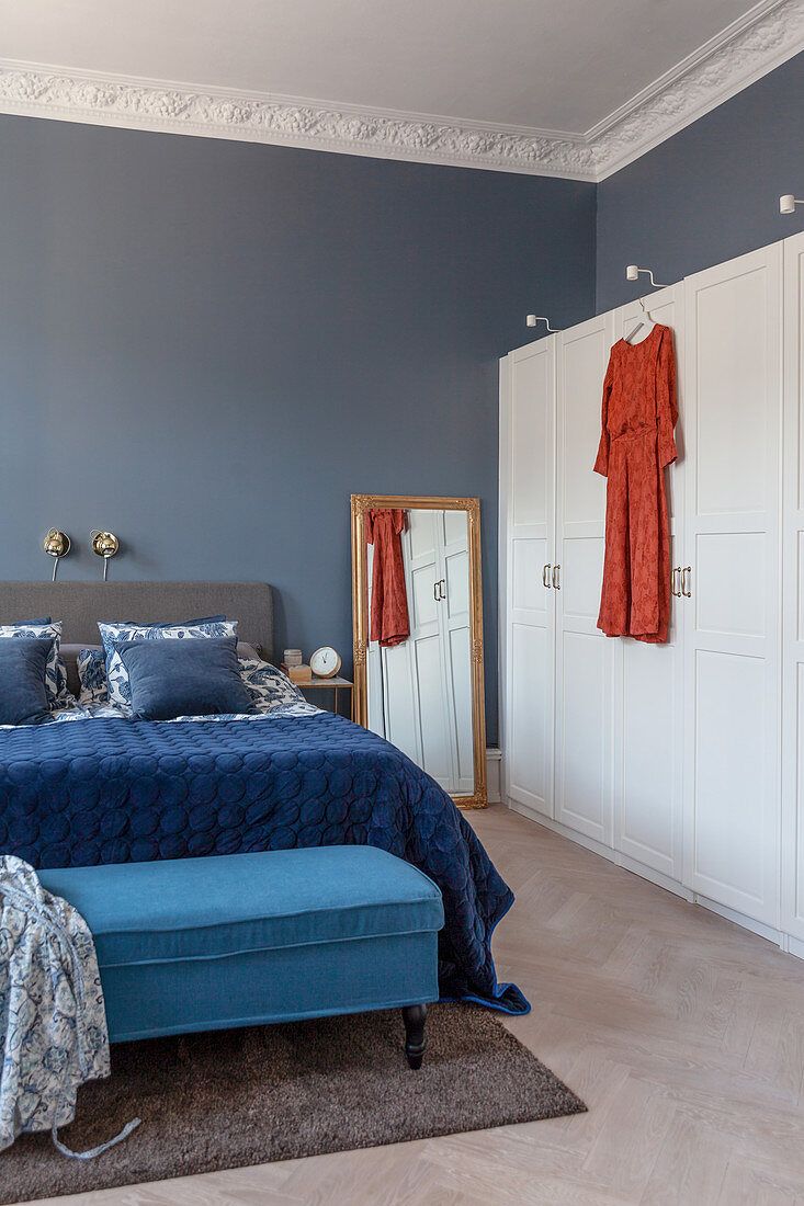 Bett mit blauem Samtüberwurf und Bettbank daneben moderner weißer Kleiderschrank
