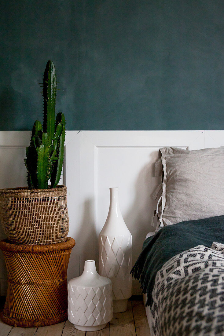 Kaktus in Korb und Vasen neben Bett im Schlafzimmer