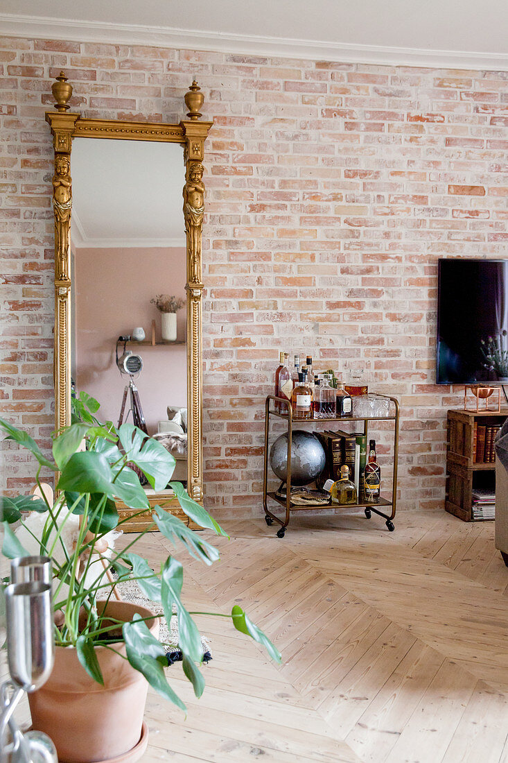 Vintage serving trolley and gilt-framed mirror against brick wall