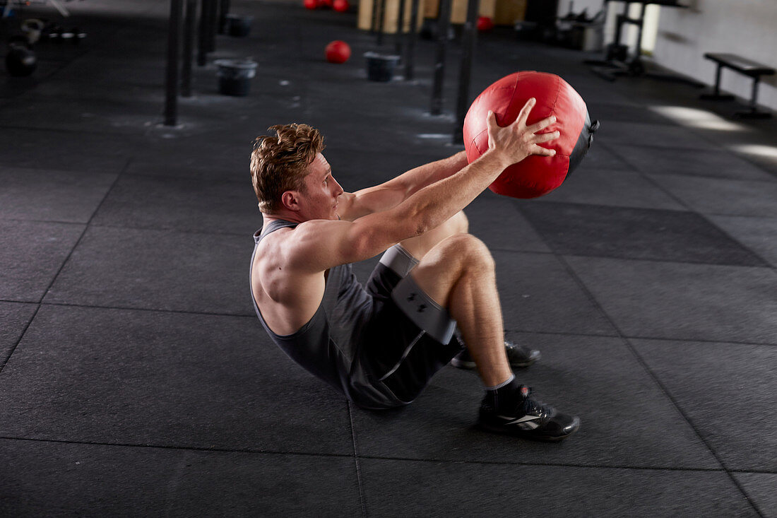 A young man performing a deck squat with a medicine ball