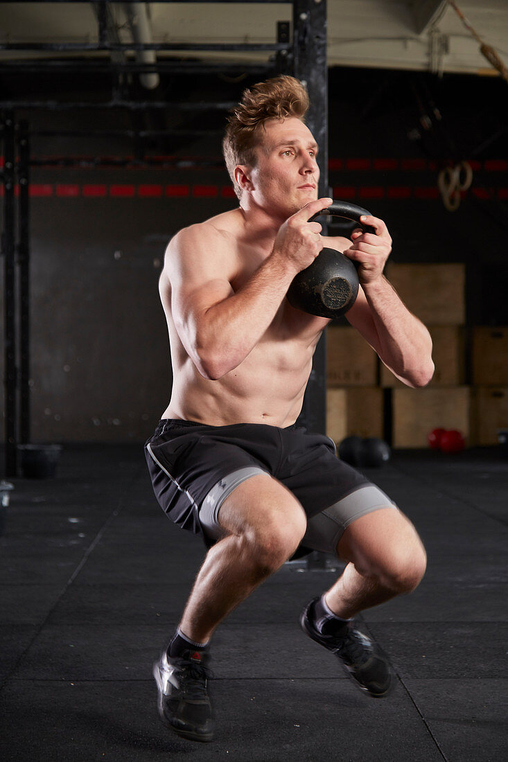 A young man performing knee jumps with a kettlebell