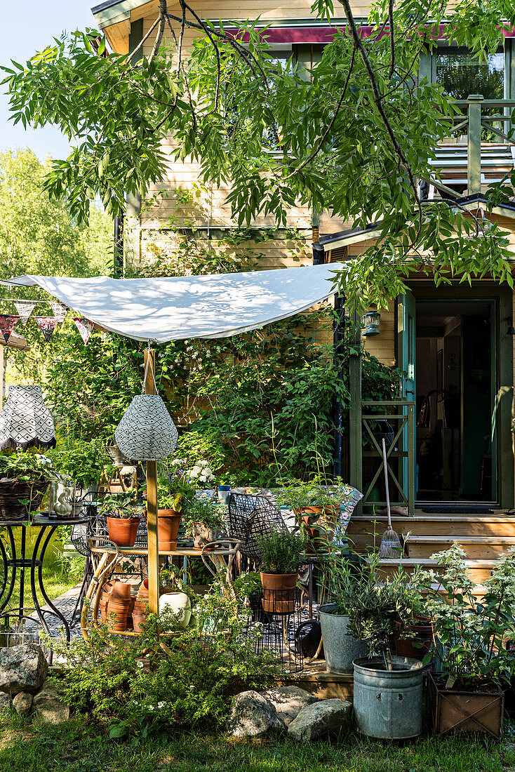 Idyllic seating area on terrace below awning in summery garden