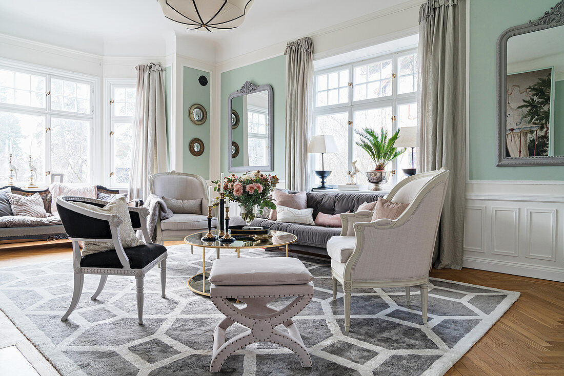 Stylish seating around round table in light-flooded living room with pastel-green walls