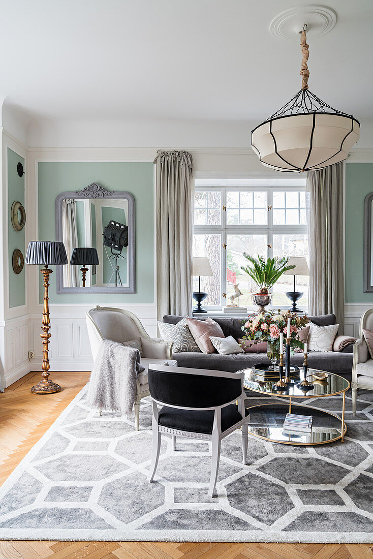 Stylish seating around round table in light-flooded living room with pastel-green walls