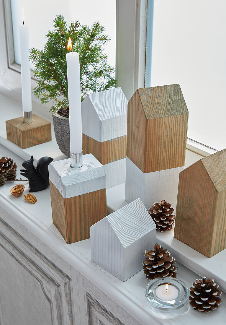Simple house-shaped ornaments and wooden candle holders on windowsill