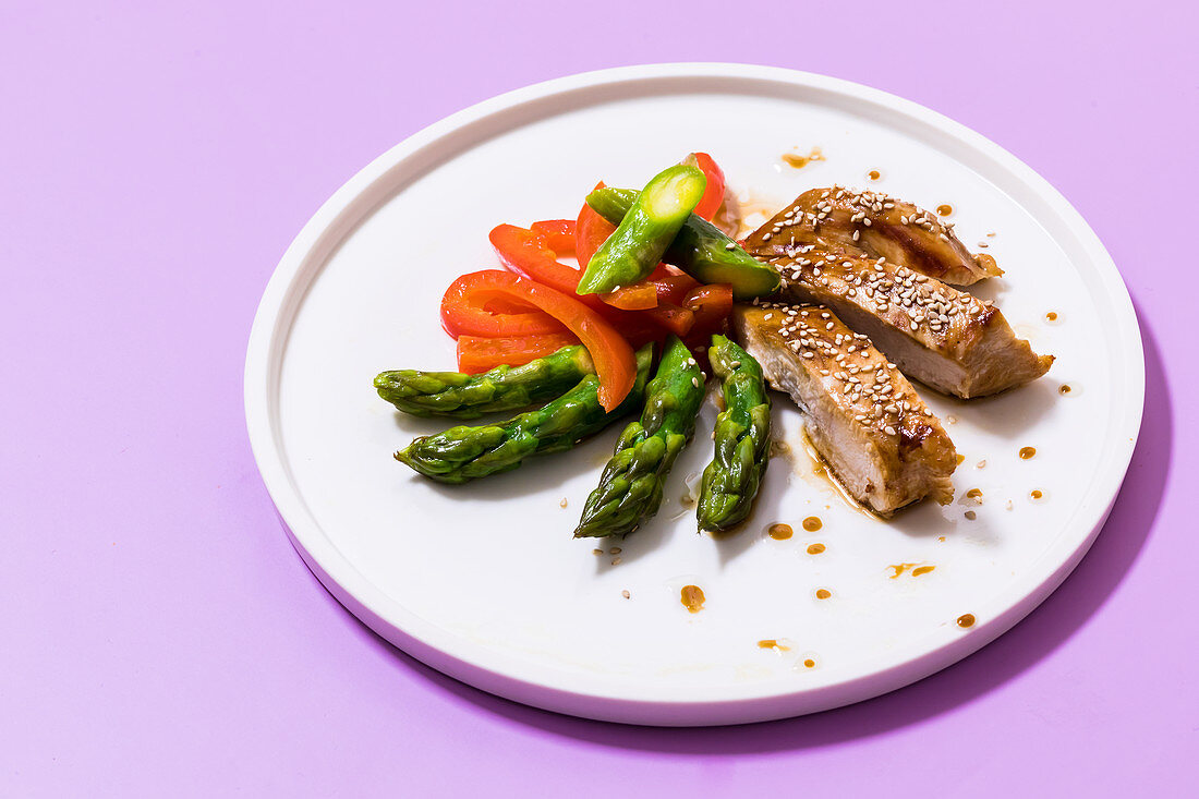 Honey and sesame seed chicken on a bed of asparagus and peppers