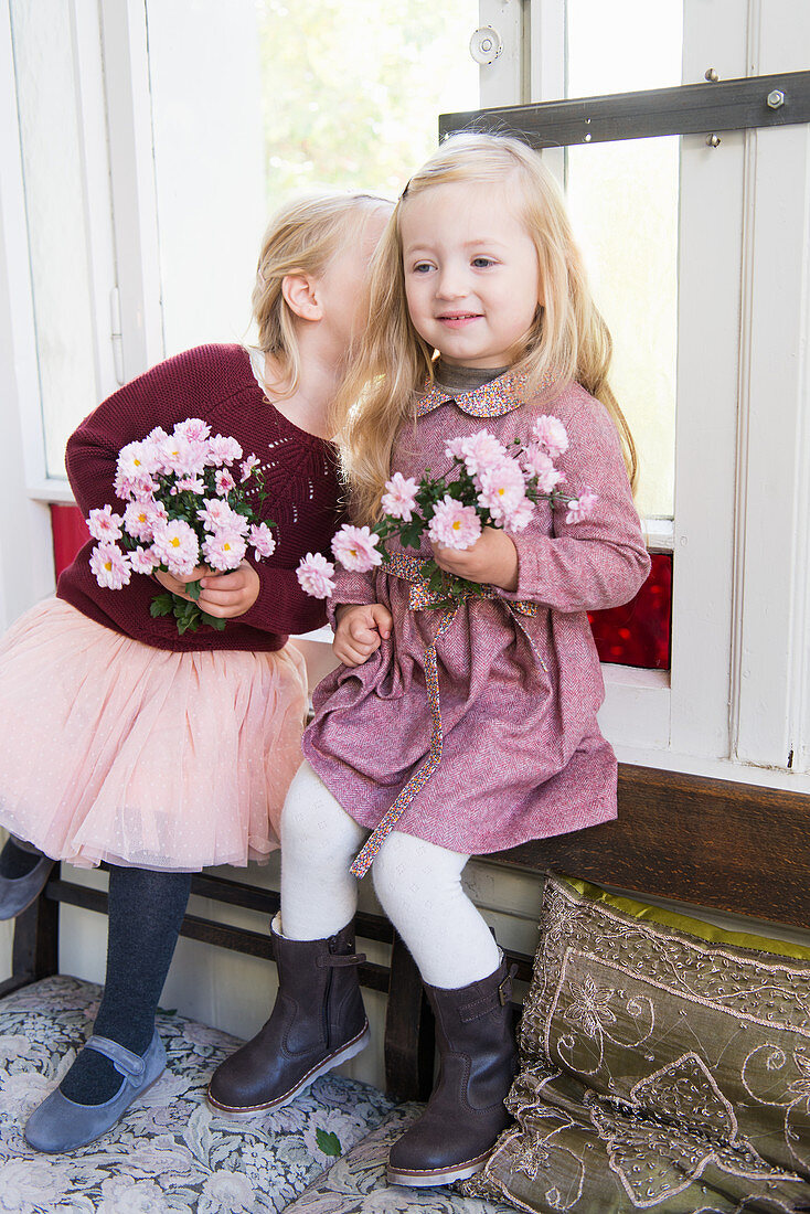 Zwei Mädchen mit Blumen flüstern