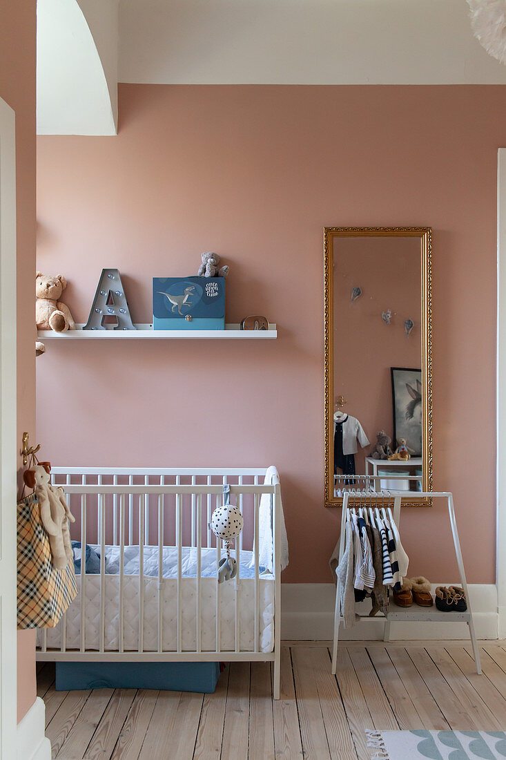 Gitterbett und kleine Garderobe im Kinderzimmer mit Wand in Rosa