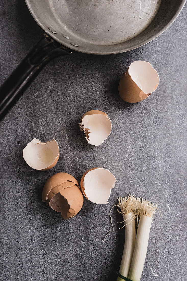 Broken eggshells and spring onions next to a pan