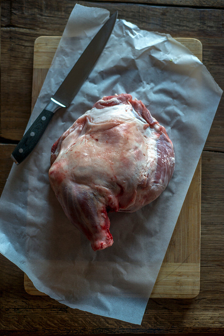 Raw lamb shoulder with a knife on parchment paper