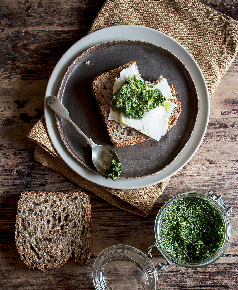 Plate with tasty rye toast with cheese and fresh pesto placed on timber tabletop