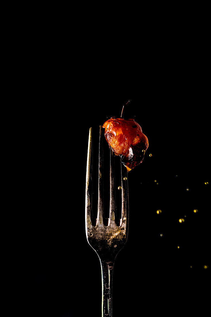 Baked cherry tomatoe on a fork, sprinkled with olive oil