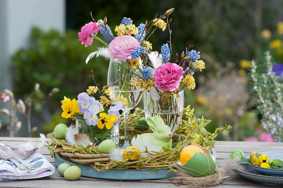 Easter table decoration with ranunculus, violets, grape hyacinths and cornelian cherry with Easter eggs and Easter bunny in a wicker wreath