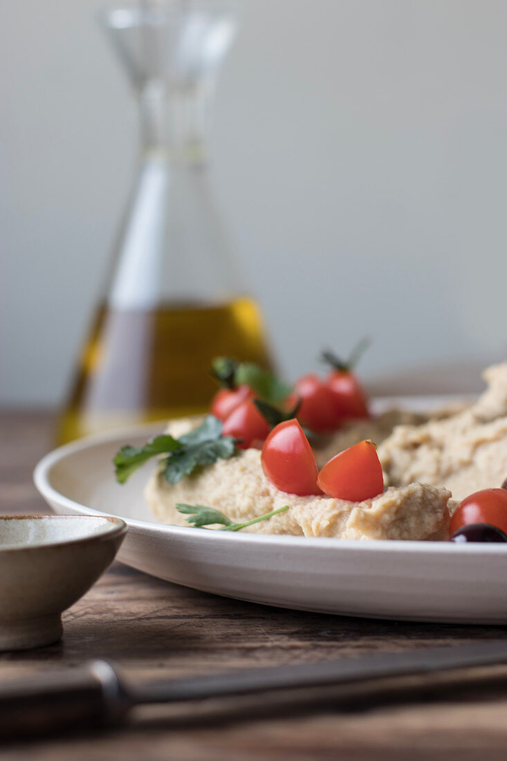 Plate of delicious pesto hummus decorated with cherry tomatoes and beans with parsley