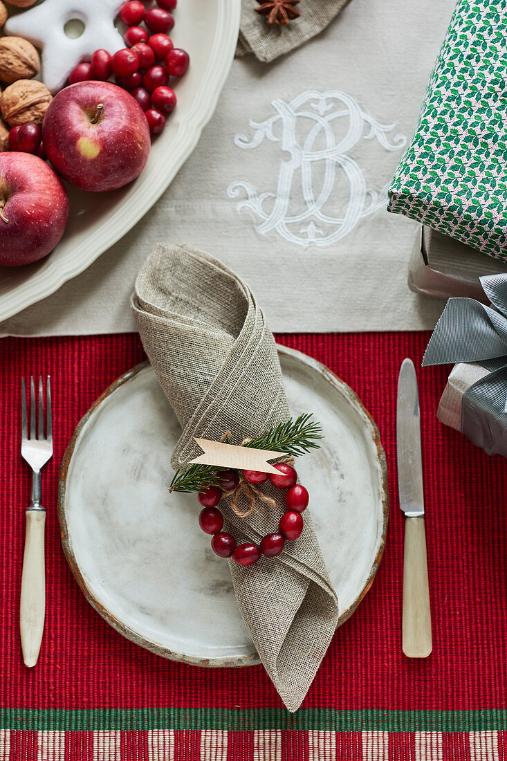 A white ceramic plate with a fork and knife beside it on a Christmas table with a red tablecloth