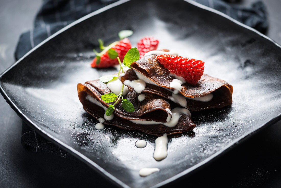Vegan chocolate crepes with vanilla sauce, strawberries and mint
