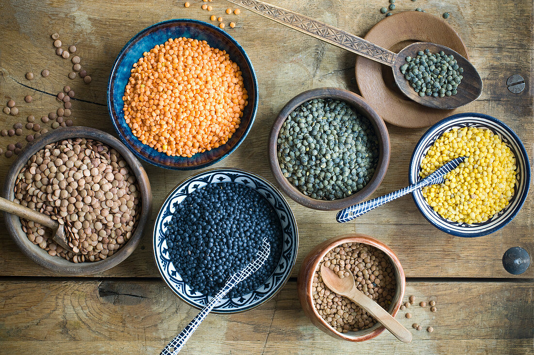 Various types of lentils in bowls on a rustic wooden surface
