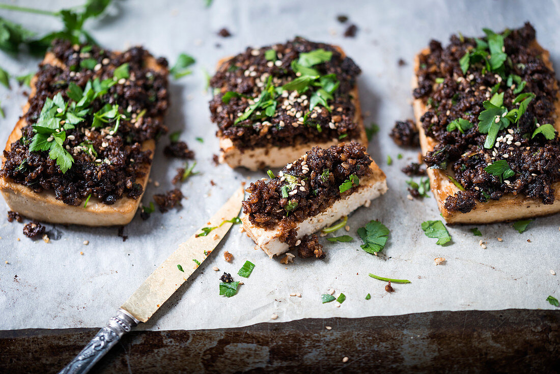 Tofu topped with black breadcrumbs, garnished with parsley and sesame seeds sliced (vegan)