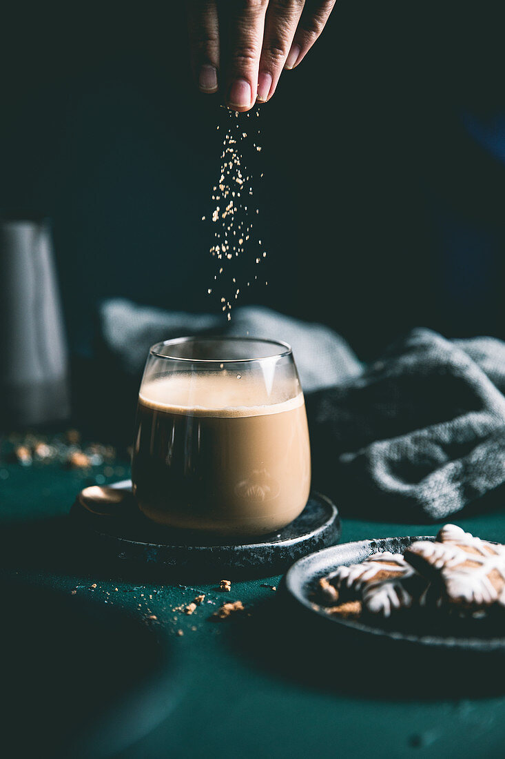 Braunen Zucker in Glas mit Milchkaffee streuen