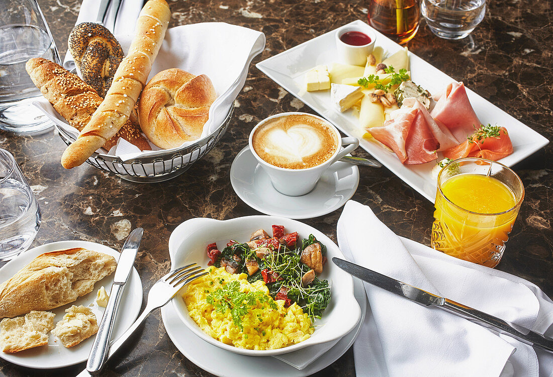 Frühstückstisch mit Rührei, Käse, Wurst, Orangensaft, Kaffee und Gebäck