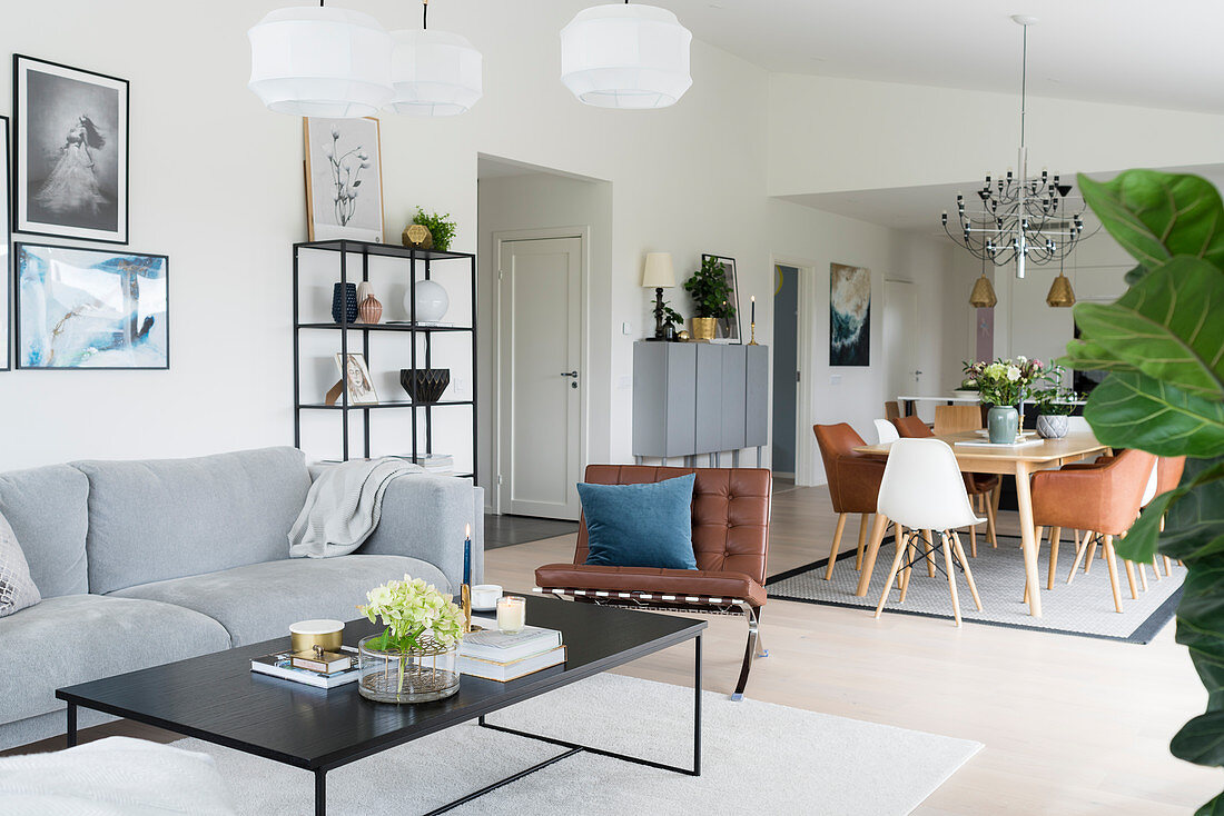 Heller offener Wohnraum mit Sofa und Couchtisch sowie Esstisch mit Klassikerstühlen im Hintergrund