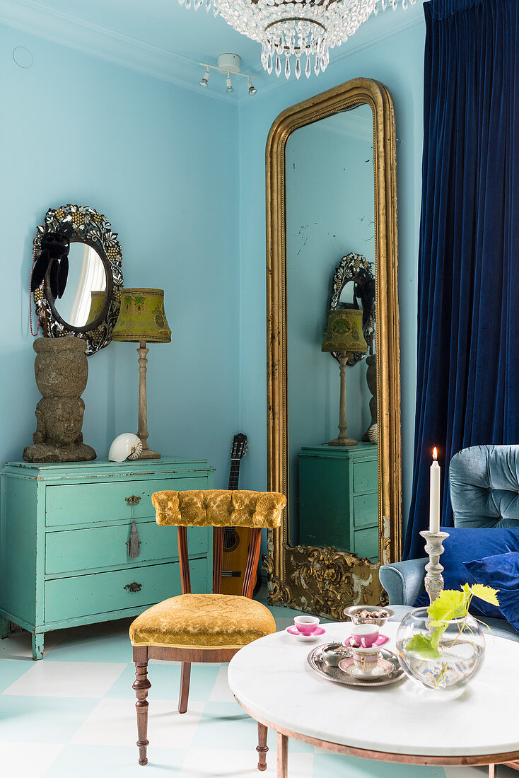 Gilt-framed mirror next to turquoise vintage chest of drawers in interior of period apartment