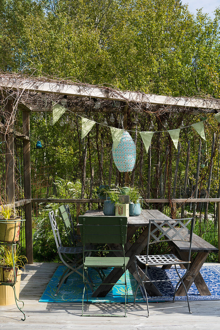 Holztisch mit Bank und Klappstühlen unter Pergola im Frühling