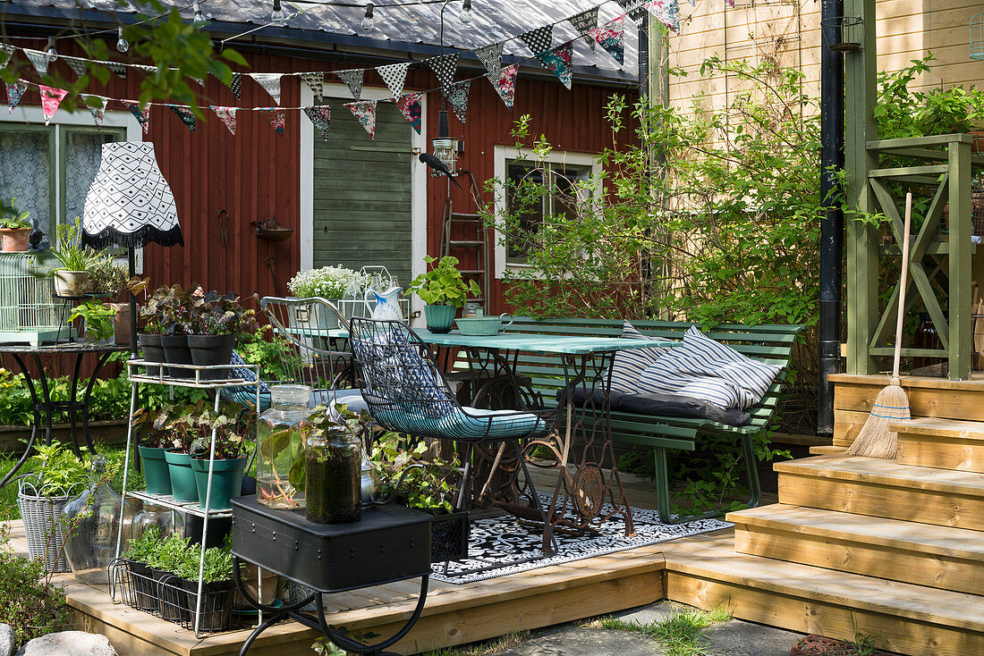 Holzterrasse dekoriert mit Pflanztöpfen und Gartenmöbeln im nostalgischen Flair