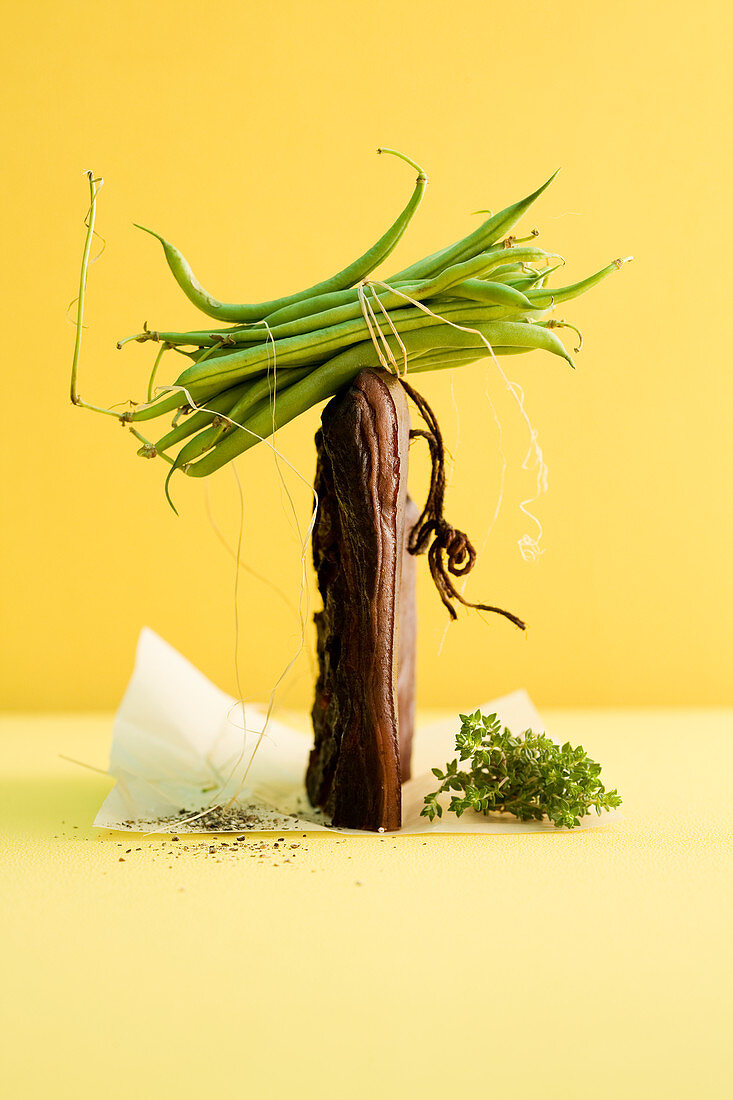 An arrangement of green beans, smoked bacon, pepper and herbs