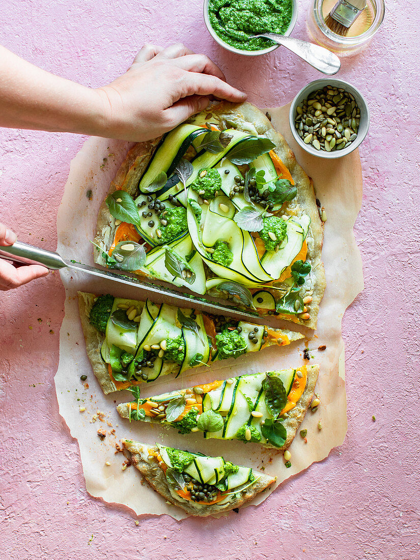 A pizza with courgette, herbs and pesto being sliced