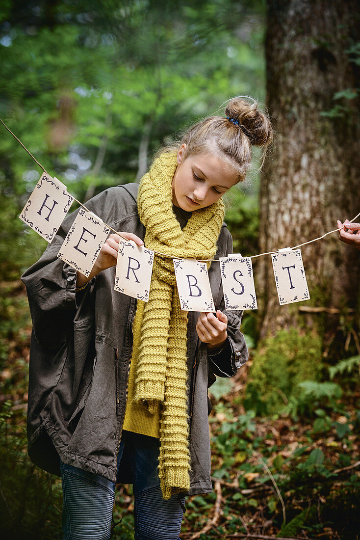 Girl hanging up autumn garland in woods