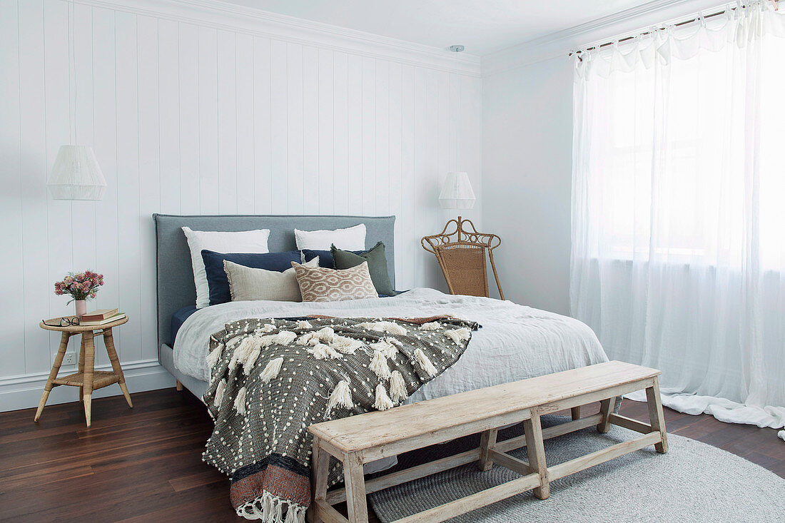 Bank vorm Bett im hellen Schlafzimmer in Weiß und Naturtönen