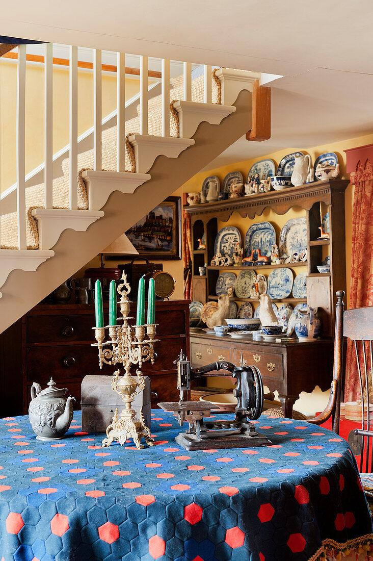 Antique sewing machine and candelabra on round table in front of old dresser crammed with crockery