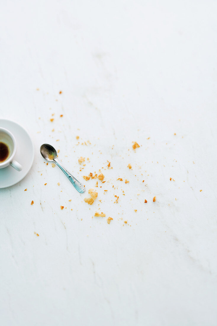 Croissiant crumbs next to an empty espresso cup