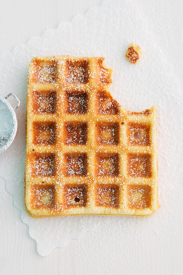 A waffle dusted with icing sugar with a bite taken out