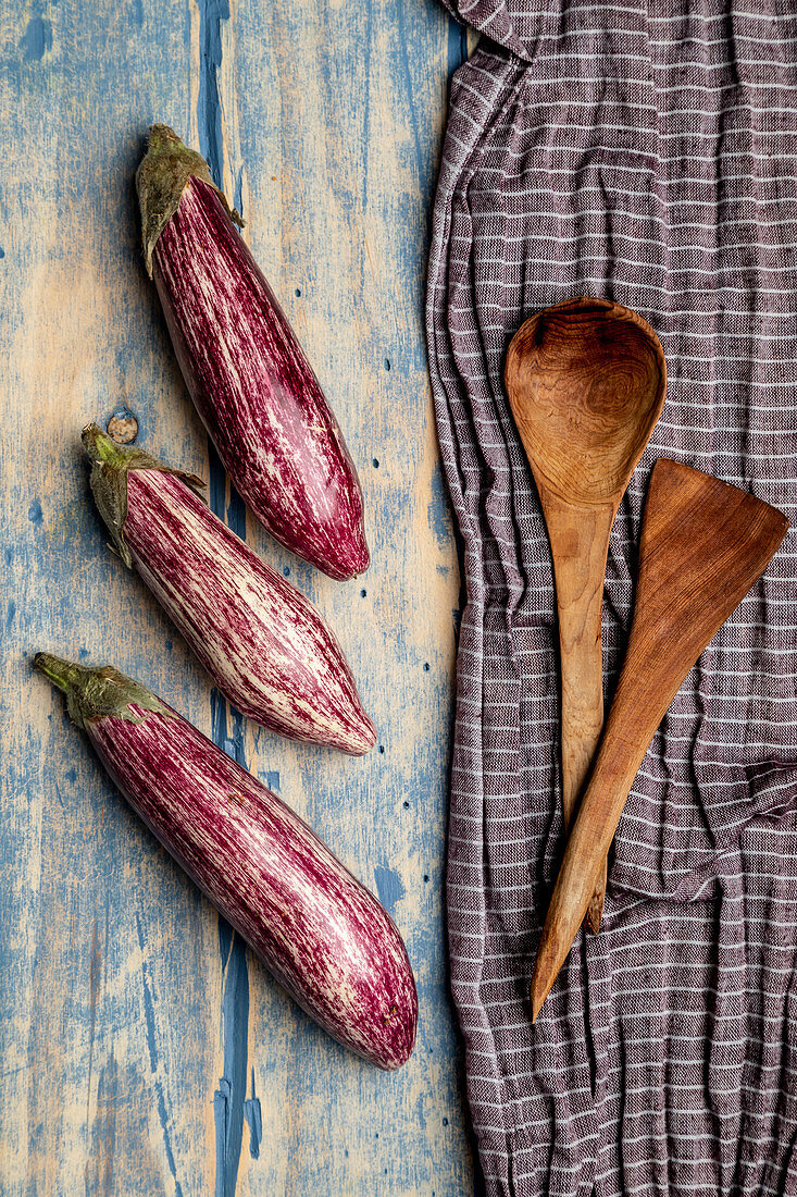 Set of fresh ripe eggplants placed near piece of striped cloth on weathered wooden tabletop