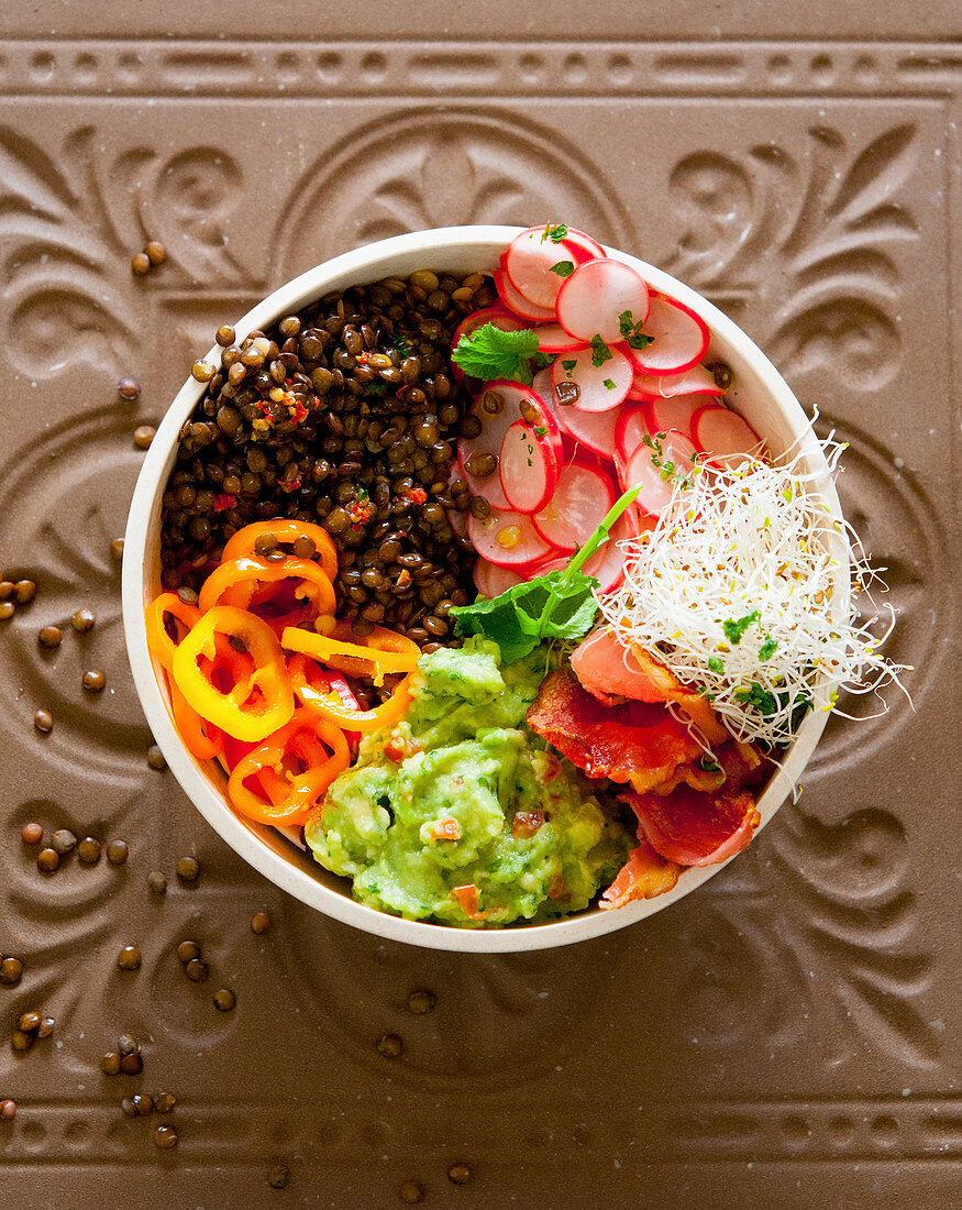 A bowl with lentils, guacamole, radishes, peppers and beansprouts