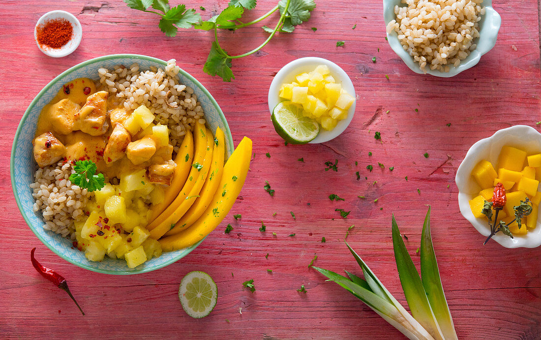 A bowl with chicken, peanut sauce, wholemeal rice, mango and pineapple