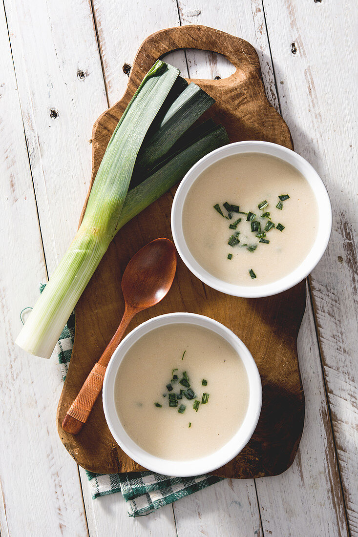 Two bowls of tasty Vichyssoise soups on wooden table with leek