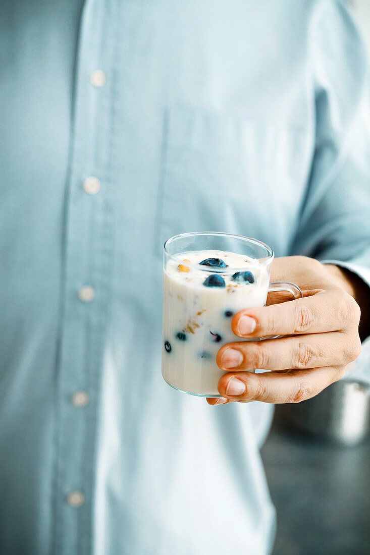 Hand hält Joghurt mit Früchten und Samen