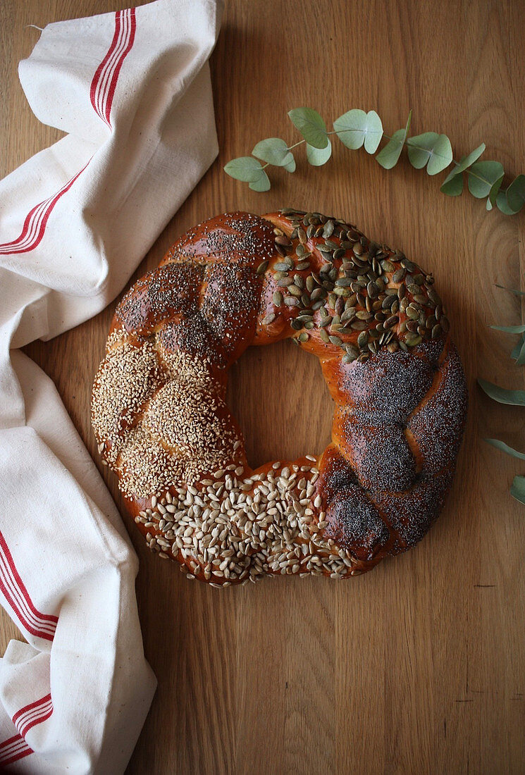 Yummy fresh challah bread with various seeds placed on lumber tabletop near cloth napkin and green plant sprig